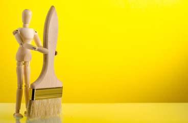 wooden man figure with paintbrush on yellow background