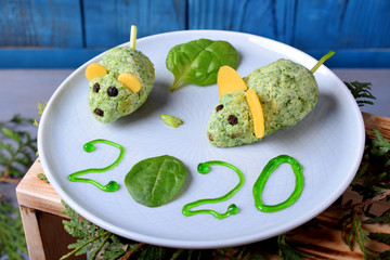 Mice of spinach and cream cheese on a ceramic plate against the blue background. Symbol of the New Year 2020