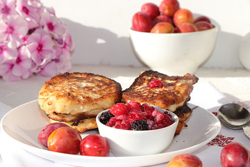 Delicious russian pancakes with cherries and strawberries and a mug of milk on a bright table, selective focus. Traditional Russian pancakes, natural food, jam and berries with milk.