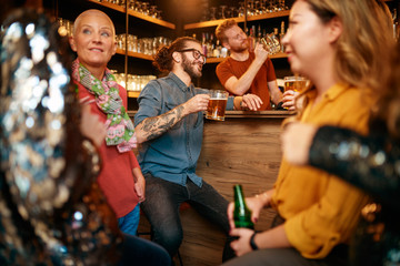 Group of friends drinking beer, chatting and having good time at pub. Night out.