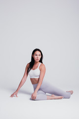 Athletic young woman doing yoga on a white background - the concept of a healthy lifestyle and a natural balance between the body and mental development, in gray leggins and white T-shirt