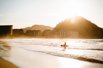 Surfer enters to the water on Zurriola Beach in San Sebastian during sunset
