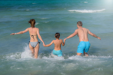 Happy European family is spending holidays on the seaside. They running to the sea smiling and holding hands.