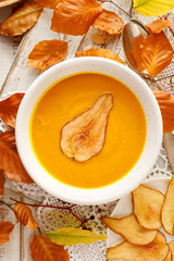 Pumpkin soup with the addition of pear chips in a white ceramic bowl, top view. Delicious and healthy vegan soup