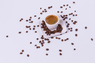 Hot coffee in a cup, coffee beans are scattered nearby. White background, top view