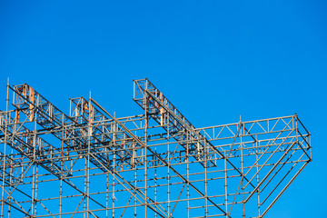 Metallic structure of assembled pipes to hold a stage, blue sky background.