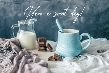 Pastel blue coffee mug, bottle of milk and chocolate on rustic table with greeting quote