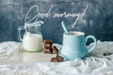 Pastel blue coffee mug, bottle of milk and chocolate on rustic table with greeting quote