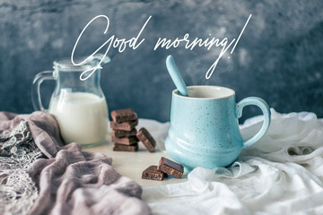 Pastel blue coffee mug, bottle of milk and chocolate on rustic table with greeting quote