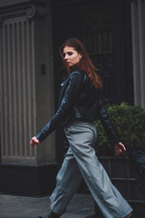 Fashion shooting. Wide trousers tube. Satin emerald blouse. Fashion trend. Tall brunette model. Black eco leather jacket.Stylish backpack made of eco leather. Handbag.