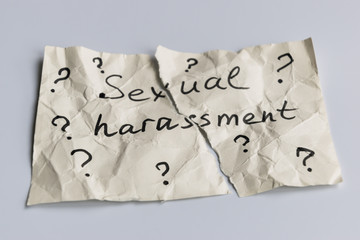 Sexual harassment concept. A torn piece of crumpled paper with many question mark signs and the words sexual harassment