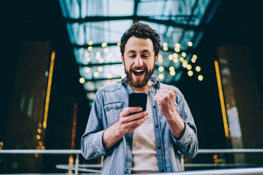 Emotional caucasian hipster guy excited with result of match victory watching video online on smartphone and 4G connection, happy millennial male overjoyed with get new free app for mobile phone .