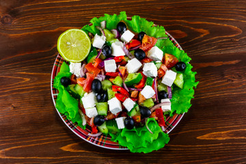 plate of tasty healthy greek salad on a blrown wooden table , national dish of Greece on a beautiful background , greek's kitchen with spices , fork and lemon