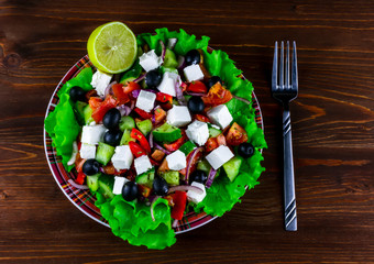 plate of tasty healthy greek salad on a blrown wooden table , national dish of Greece on a beautiful background , greek's kitchen with spices , fork and lemon