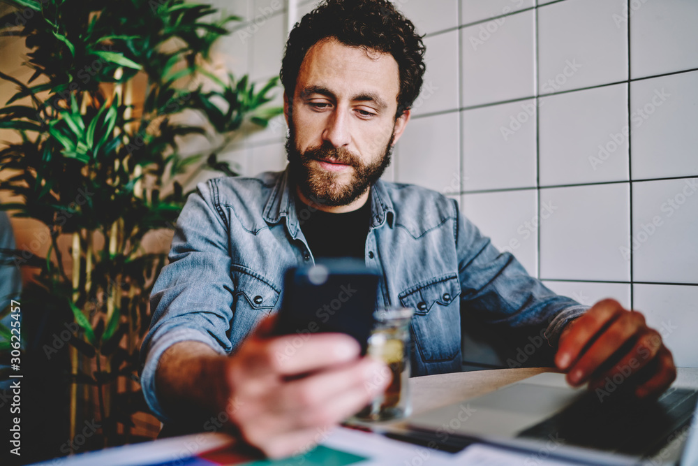 Poster handsome caucasian hipster guy checking mail and notification on mobile phone on break in cafe, pens