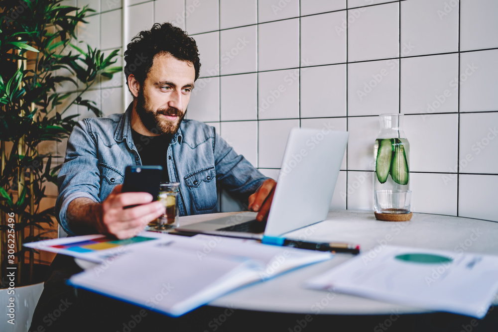Poster skilled male freelancer installing app on smartphone for synchronizing files with laptop computer,yo