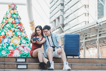 Couples Asian tourists using mobile phones Take a selfie While they wait for the electric train on station with blur  christmas tree and  building background concept to couples traveling on holiday.