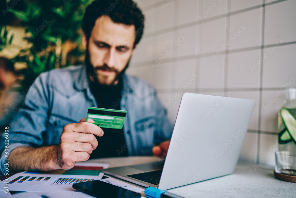 Poster selective focus on credit banking card, hipster guy sitting on blurred background making shopping in