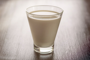 Milk in a glass cup on a wooden background. Photographed close-up in a low key.