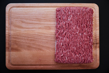 Raw minced pork on wooden cutting board on black background close-up. top view, copy space left