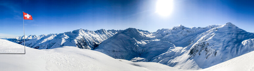 Fototapeta na wymiar swiss alps mountain range in winter with blue sky and switzerland national flag