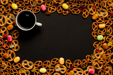 Cup of coffee among pile of various печенья and multicolored caramelon black wooden background. Top view.