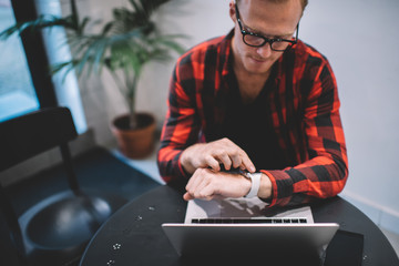 Male freelancer checking smartwatch in cafe