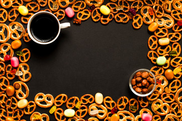 Cup of coffee among pile of various cookies, almonds in glass transparent bowland multicolored caramelon black wooden background. Top view.