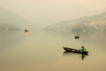 Pokhara, Nepal - March 12, 2014: The calm and quiet Lake Feva at sunset is the main attraction of the city of Pokhara. The nature of Nepal. Simple wooden fishing boats with fishermen sail on the lake.