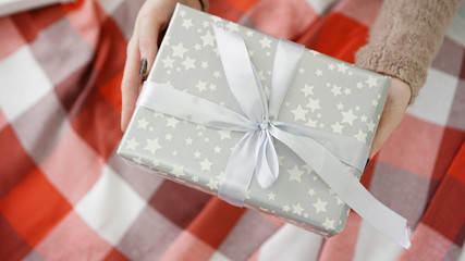 Unpacking Christmas silver presents. Woman holds and opening presents on warm white and red plaid