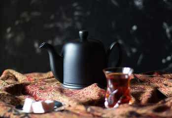 Black teapot and traditional tea glass armudu on scarf with asian pattern