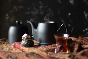 Obraz na płótnie Canvas Black teapot, sweets and traditional tea glass armudu on scarf