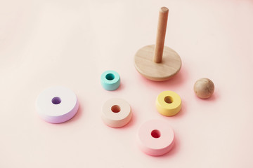 Eco friendly, plastic free toys for toddler. Stylish wooden toys for child on pink background, flat lay. Modern colorful wooden pyramid with disassembled rings.