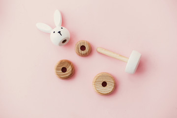 Eco friendly, plastic free toys for toddler. Stylish wooden toys for child on pink background, flat lay. Modern colorful wooden bunny pyramid with disassembled rings.