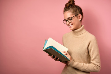 A girl with clean skin and a high bun in glasses stands in a half-turned and looks at the open book with a smile