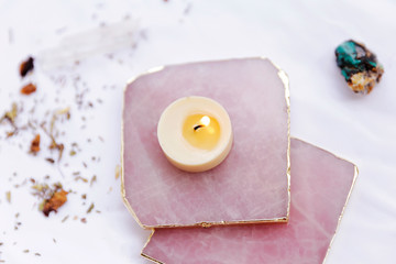 Rose quartz coasters with candle on the white background. Gentle meditative concept. Spa and wellness theme. 