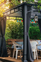 Little colorful lampions hanging on a pavilion in a garden on a sunny summer day. Cozy Chairs and Table standing underneath it.