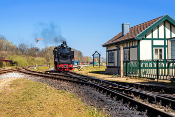 Fototapeta na wymiar Schmalspurbahn, Dampflok bei Einfahrt in Bahnhof mit Signal und Wartehäuschen