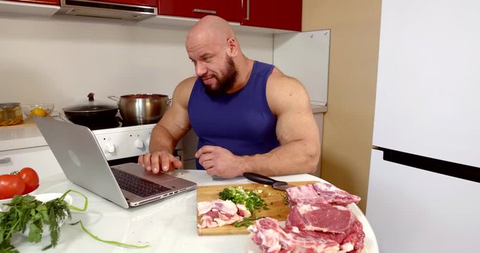 sportsman works with laptop at kitchen table with raw meat