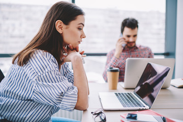 Caucasian woman concentrated on making online research for business using laptop computer in modern office, serious female entrepreneur watching video via application on netbook for browsing internet