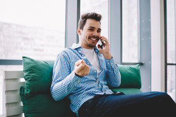 Happy smiling male calling to friend for communicating and discussing time for meeting using 4g wireless internet connection for making smartphone conversation indoors during leisure on cozy couch