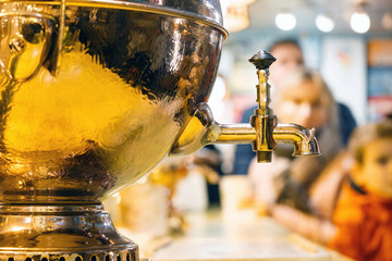 Samovar - a Russian kettle for boiling water of gold color on a background with people.