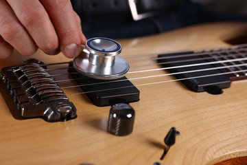 Male arms hold stethoscope head diagnosing guitar