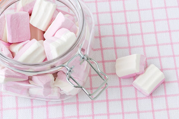White pink fluffy marshmallows in a clip top glass jar on a checkered tablecloth. Sweet and tasty winter food. Close-up delicious soft sweets.