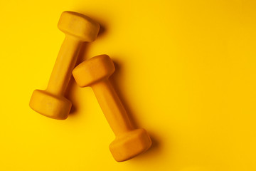 yellow dumbbells lie on a yellow background, the concept of summer, training, sports