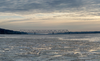 cracked ice on the river at sunset. beautiful clouds. railroad bridge