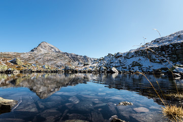 Reflection of mountain peak in clear fresh water of alpin pond after first snow close to Lago Bianco at Bernina pass Switzerland