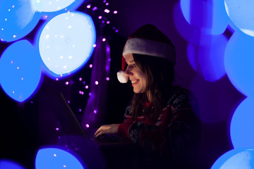 young girl with a laptop in the New Year sits at home in Christmas clothes, a woman online for Christmas
