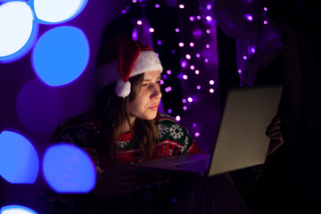 girl student in Christmas clothes sits at home with a laptop at night, a lonely woman meets a holiday online, she use a computer for Christmas