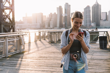 Fototapeta premium Concept of discover country and visit international city of America, positive female travel blogger typing text for social publication while networking and messaging with followers via cellphone